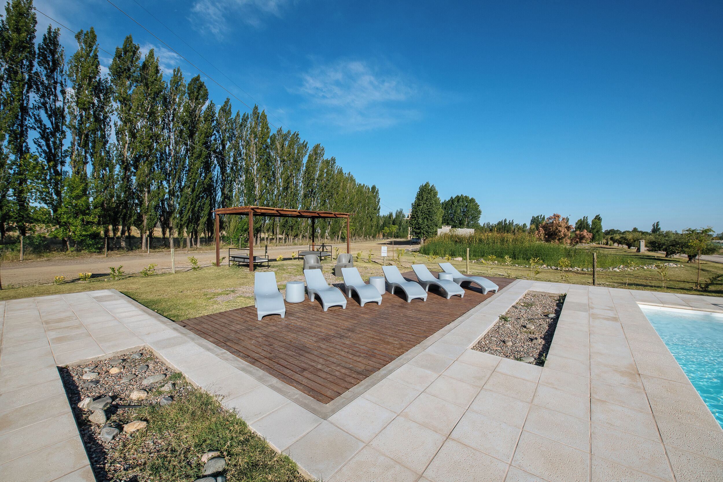 Un espace aménagé au bord de la piscine, avec des chaises longues, une terrasse en bois et une pergola.