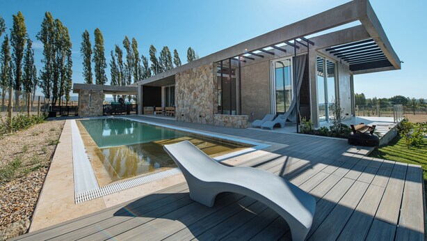 Ein modernes Haus mit Swimmingpool, Sitzgelegenheit im Freien und einer Steinmauer.