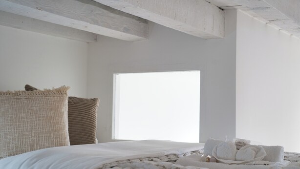 A bedroom with a large window, a bed with white linens, and a small bedside table with towels. - Cozy Navigli Loft - One Bedroom Apartment, Sleeps 2 (Milano)