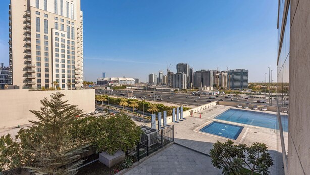 A high-rise building with a swimming pool and a view of a cityscape. - Stayshort - Stylish 1-bedroom Home Fully Furnished in JVC (Dubai)