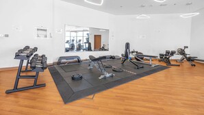 A gym with exercise equipment, a mirror, and a wooden floor. - Stayshort - Stylish 1-bedroom Home Fully Furnished in JVC (Dubai)