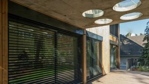 A covered outdoor area with a wooden deck, large black roller shutters, and circular skylights.