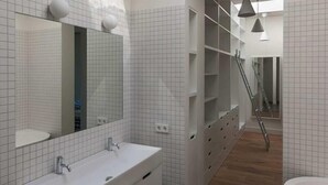 A modern bathroom with a large mirror, two sinks, a bathtub, and a skylight.