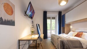 Un dormitorio con cama, escritorio, silla, televisión y ventana con cortinas.