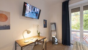 Una habitación con escritorio, silla, televisor, planta en maceta y espejo.