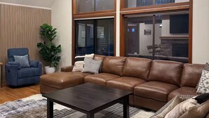 Ein geräumiges Wohnzimmer mit einem großen Ecksofa, einem dunklen Couchtisch und einer modernen Pendelleuchte.