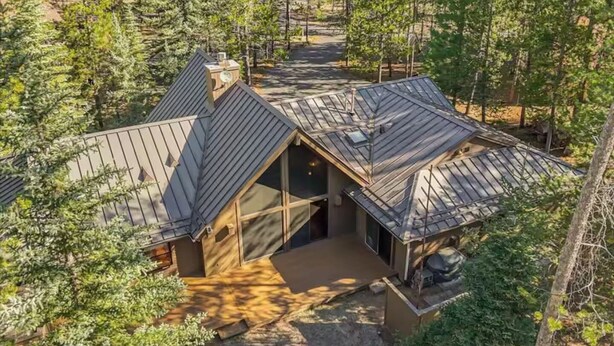Eine Hütte mit geneigtem Dach, großen Fenstern und einer überdachten Veranda, umgeben von dichtem Wald.