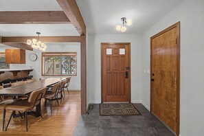 A dining area with a wooden table and chairs, a wooden door, and a ceiling light fixture. - Modern Sunriver Retreat – Sleeps 16 (Sunriver)