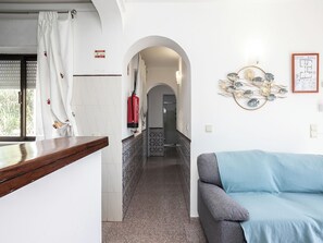 A corridor with a kitchen area, a grey sofa, and a decorative wall piece. - Dappan White Apartment, Burgau, Algarve (Burgau)