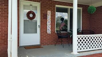 A brick house with a white porch, a door with a wreath, and a sign that says 'Give Thanks.'
