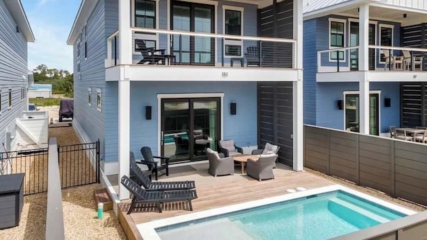 Una casa de dos pisos con balcón, piscina y mobiliario exterior.