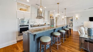 Una cocina moderna con una isla central, taburetes de bar y un comedor con sofá y mesa.