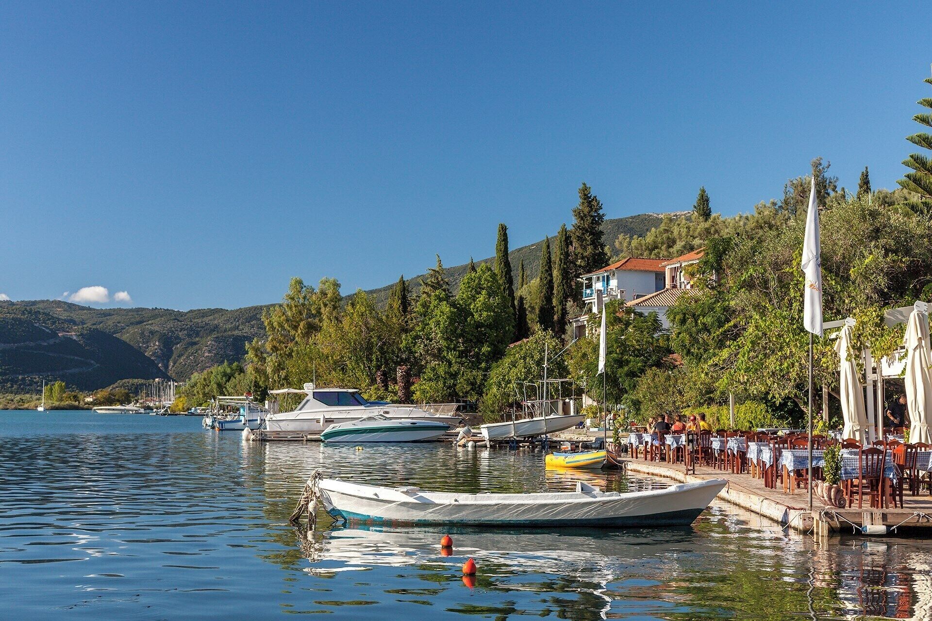 A marina with boats docked, a restaurant with outdoor seating, and a mountainous backdrop.