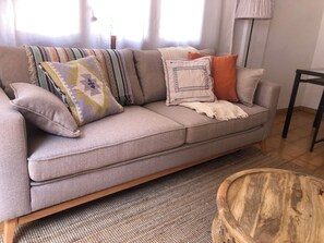 A beige sofa with multiple pillows and a throw blanket, a wooden coffee table, and a lamp in a room with a tiled floor. - Apartment with garden. Two minutes walk from the beach (Platja d'Aro)