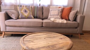 Ein beiges Sofa mit gemusterten Kissen und einem runden Couchtisch aus Holz mit Rautenmuster.