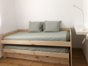 A single-bed room with a wooden frame, a green mattress, two pillows, a bedside table, and a lamp. - Apartment with garden. Two minutes walk from the beach (Platja d'Aro)