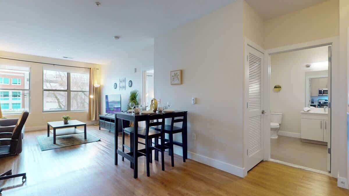 A modern living room with a dining area, hardwood flooring, and large windows.