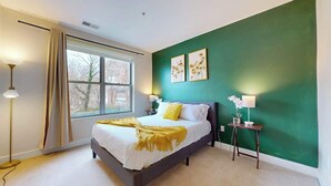 Un dormitorio con cama, ventana, pared verde y dos mesitas de noche con lámparas.
