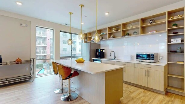 Una cocina moderna con una isla central, luces colgantes y estanterías empotradas.