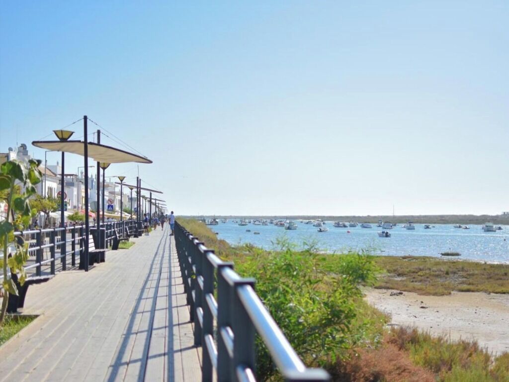 A seaside promenade with a wooden walkway, metal railings, and street lamps.
