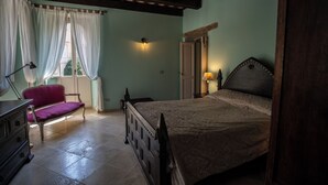 Een slaapkamer met een bed, een stoel, een dressoir en een raam met gordijnen.