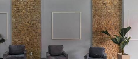 A lobby with three grey armchairs, a stone wall, and a large potted plant.