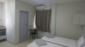 Quarto de hotel com cama, escrivaninha, cadeira e aparelho de ar condicionado.
