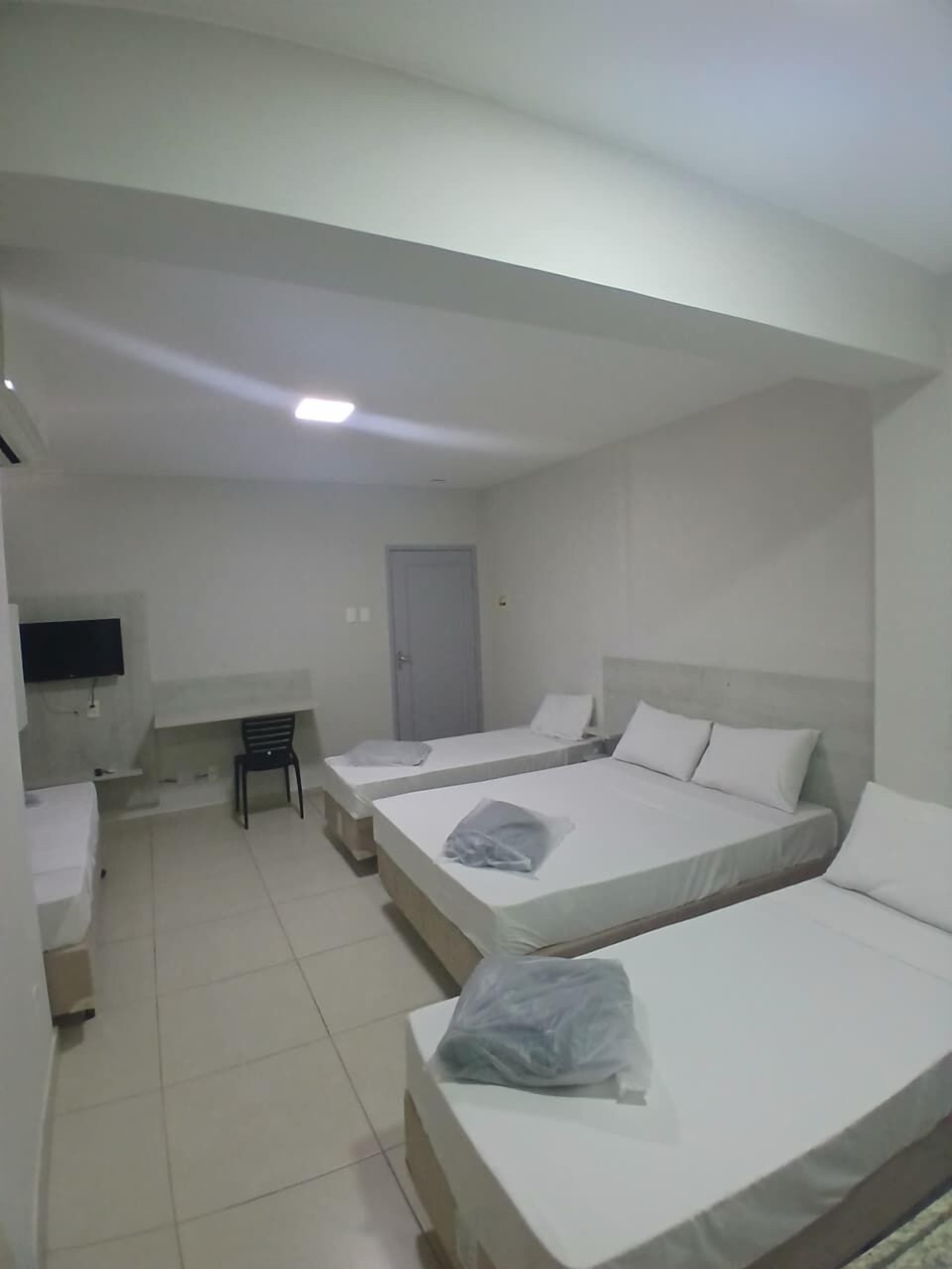 Een hotelkamer met twee eenpersoonsbedden, een bureau, een stoel en een televisie aan de muur.