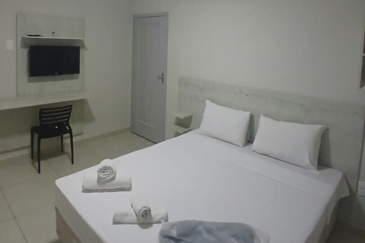 A hotel room with a bed, a television, a chair, and a door.