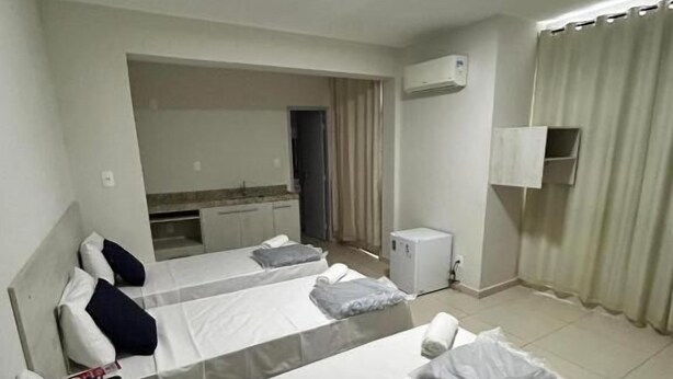 A hotel room with two beds, a small kitchenette, a bathroom, and a curtain. - GoldMen Express Campos dos Goytacazes (Campos)