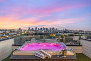 En takterrass med bubbelpool, champagne och utsikt över staden i solnedgången.