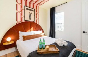 A hotel room with a large bed, a headboard, a bedside table with a lamp, a framed picture on the wall, and a window with curtains. - Fall in Nashville: hot tub, 4BR sleeps 12, garage parking, pet friendly (Nashville)