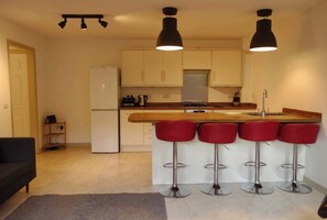 A modern kitchen with a central island, bar stools, and pendant lighting. - Modern Garden 1BDR Flat in Forest Hill Honor Oak (Greater London)