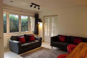 A living room with two sofas, a wooden table, and a large window with curtains. - Modern Garden 1BDR Flat in Forest Hill Honor Oak (Greater London)
