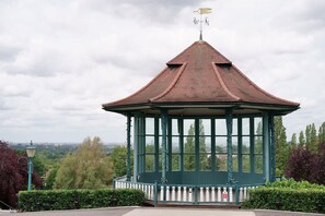 A gazebo with a pointed roof and a weather vane, surrounded by greenery and a cityscape in the background. - Modern Garden 1BDR Flat in Forest Hill Honor Oak (Greater London)