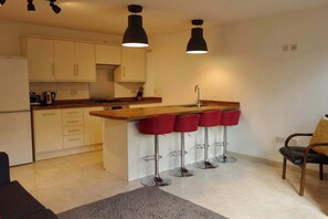 A modern kitchen with a central island, bar stools, and pendant lighting. - Modern Garden 1BDR Flat in Forest Hill Honor Oak (Greater London)