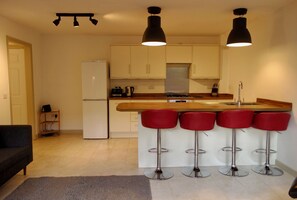 A compact kitchen with a refrigerator, stove, and bar stools. - Modern Garden 1BDR Flat in Forest Hill Honor Oak (Greater London)