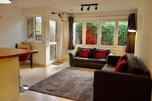 A living room with a sofa, a dining area with a table, and a window with curtains. - Modern Garden 1BDR Flat in Forest Hill Honor Oak (Greater London)