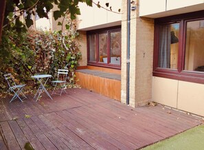 A wooden deck with a bench and a table, surrounded by a brick wall and a climbing plant. - Modern Garden 1BDR Flat in Forest Hill Honor Oak (Greater London)