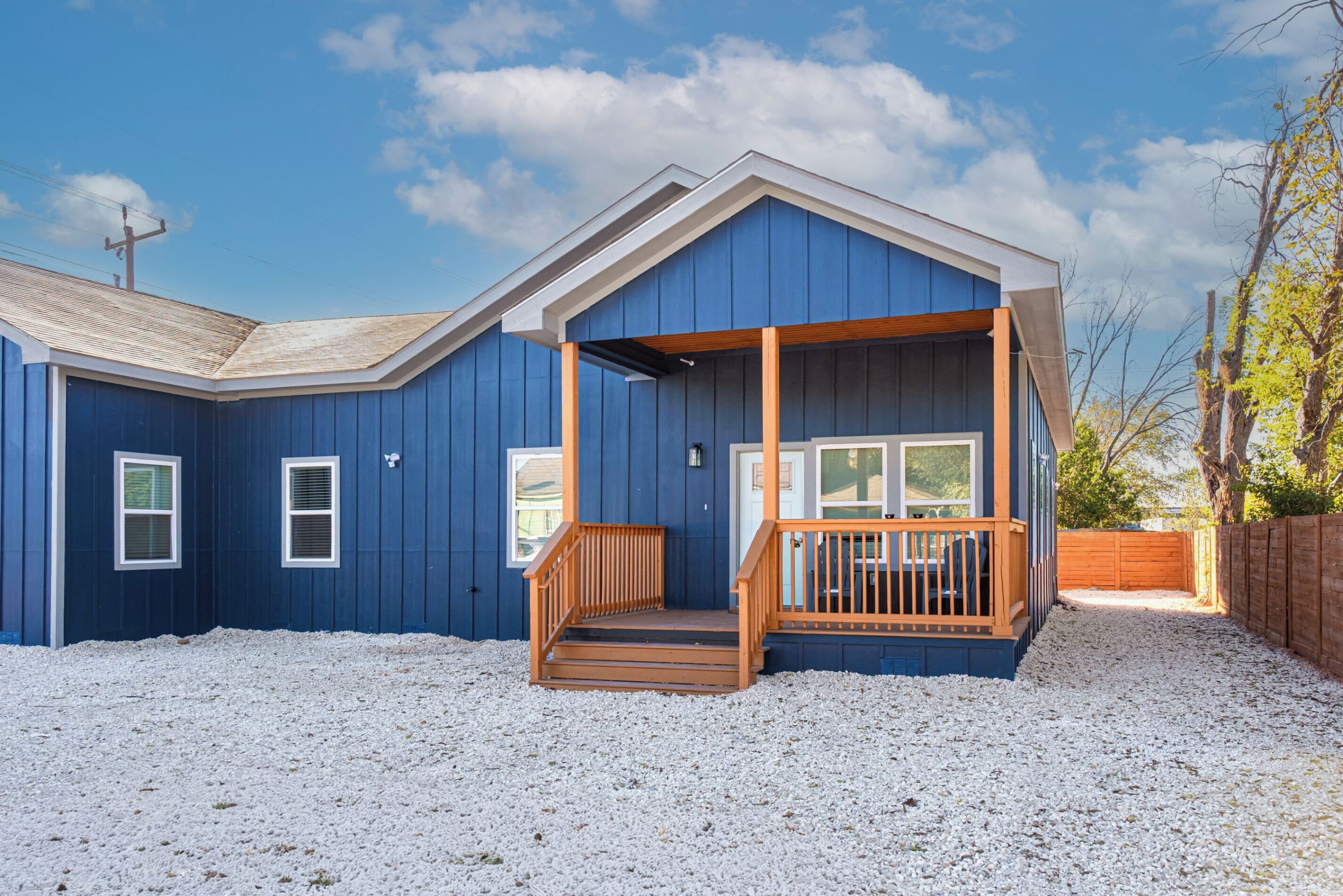 A blue house with a wooden porch and a gravel driveway.