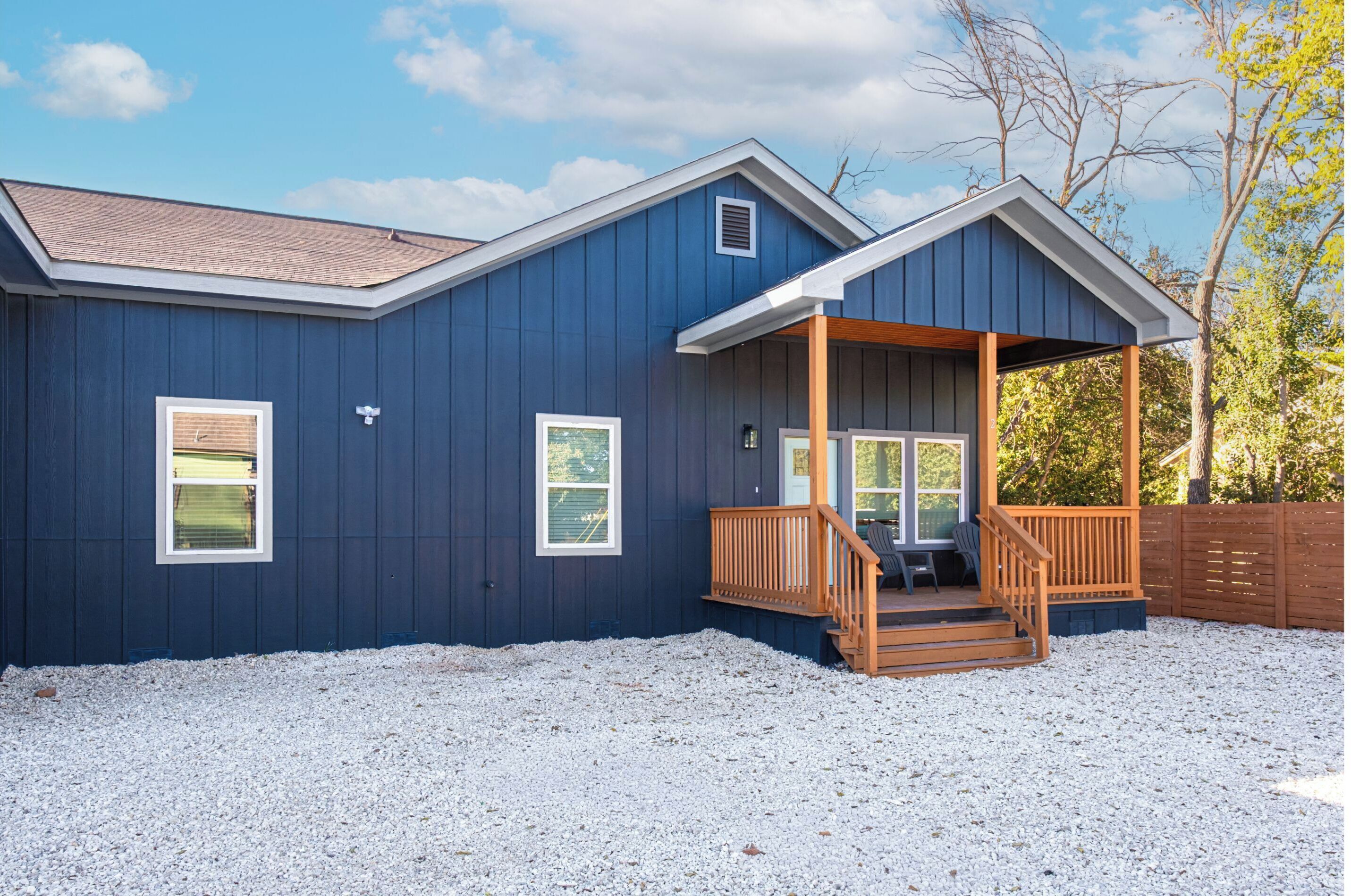 A two-story building with a dark blue exterior, a wooden deck, and a gravel driveway.