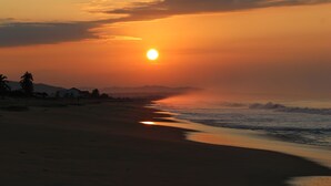 Ein Strand bei Sonnenuntergang, wolkenloser Himmel, ruhiges Meer und ferne Berge.