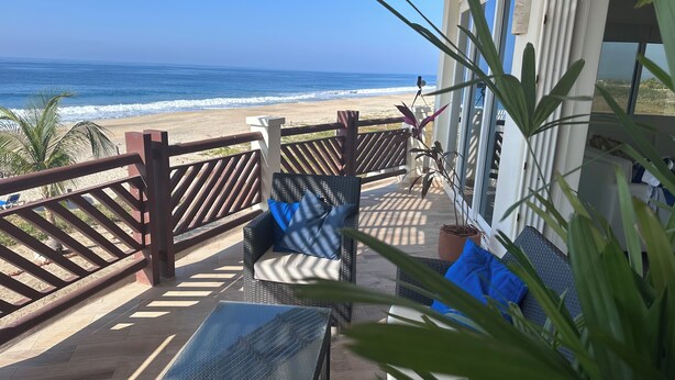 Ein Balkon mit Korbmöbeln, Blick auf den Strand und Holzgeländer.