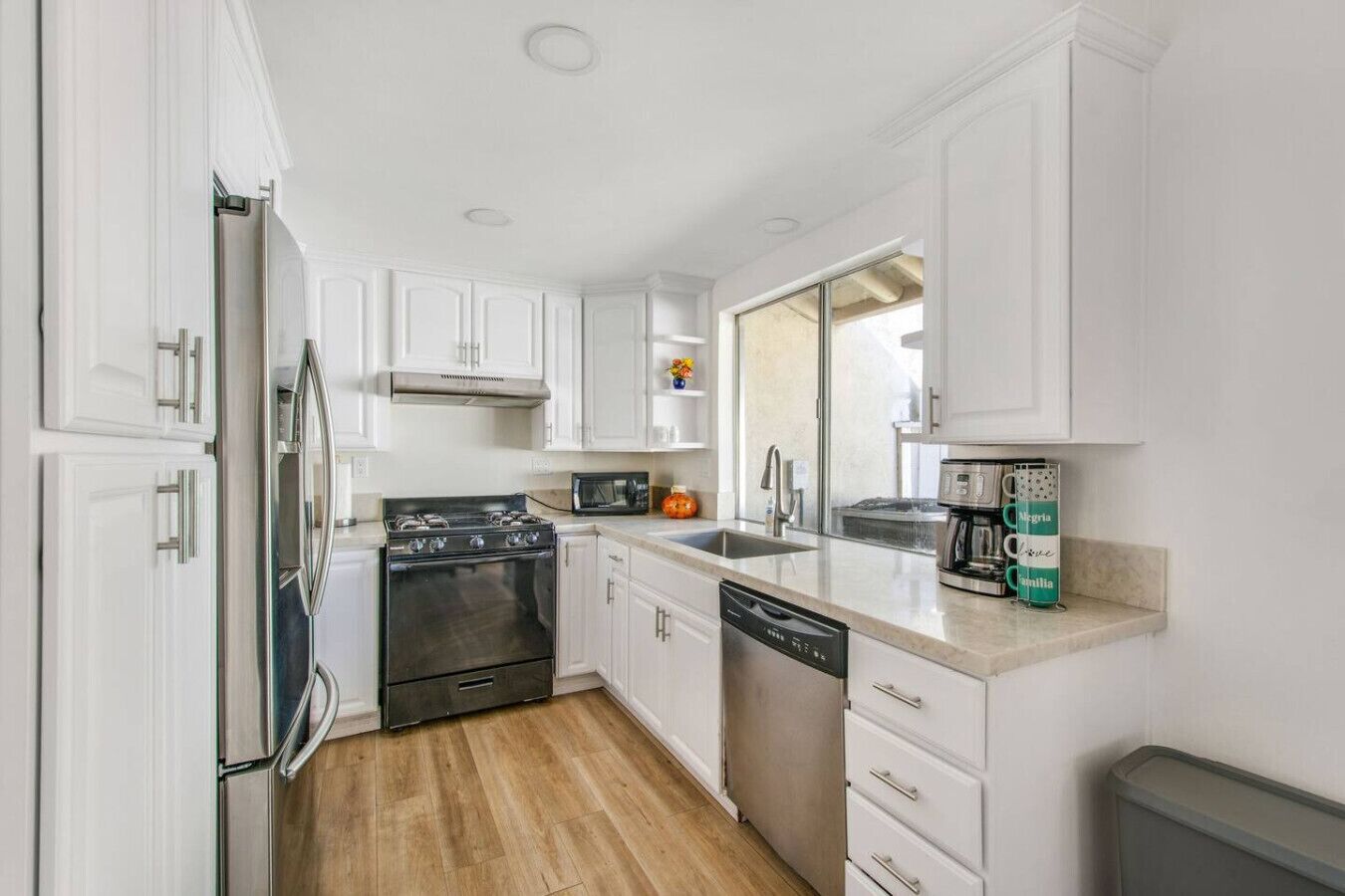 A compact kitchen with white cabinetry, a stove, microwave, and dishwasher.