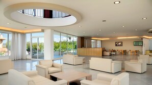 A spacious lobby with a central seating area, a reception desk, and large windows offering views of greenery. - The Garden Studio Pool View (Chania)