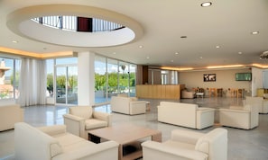A spacious lobby with a central seating area, a reception desk, and large windows offering views of greenery. - The Garden Studio Pool View (Chania)