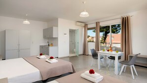 A hotel room with two beds, a kitchenette, a dining area with a table and chairs, and a balcony with a view. - The Garden Studio Pool View (Chania)