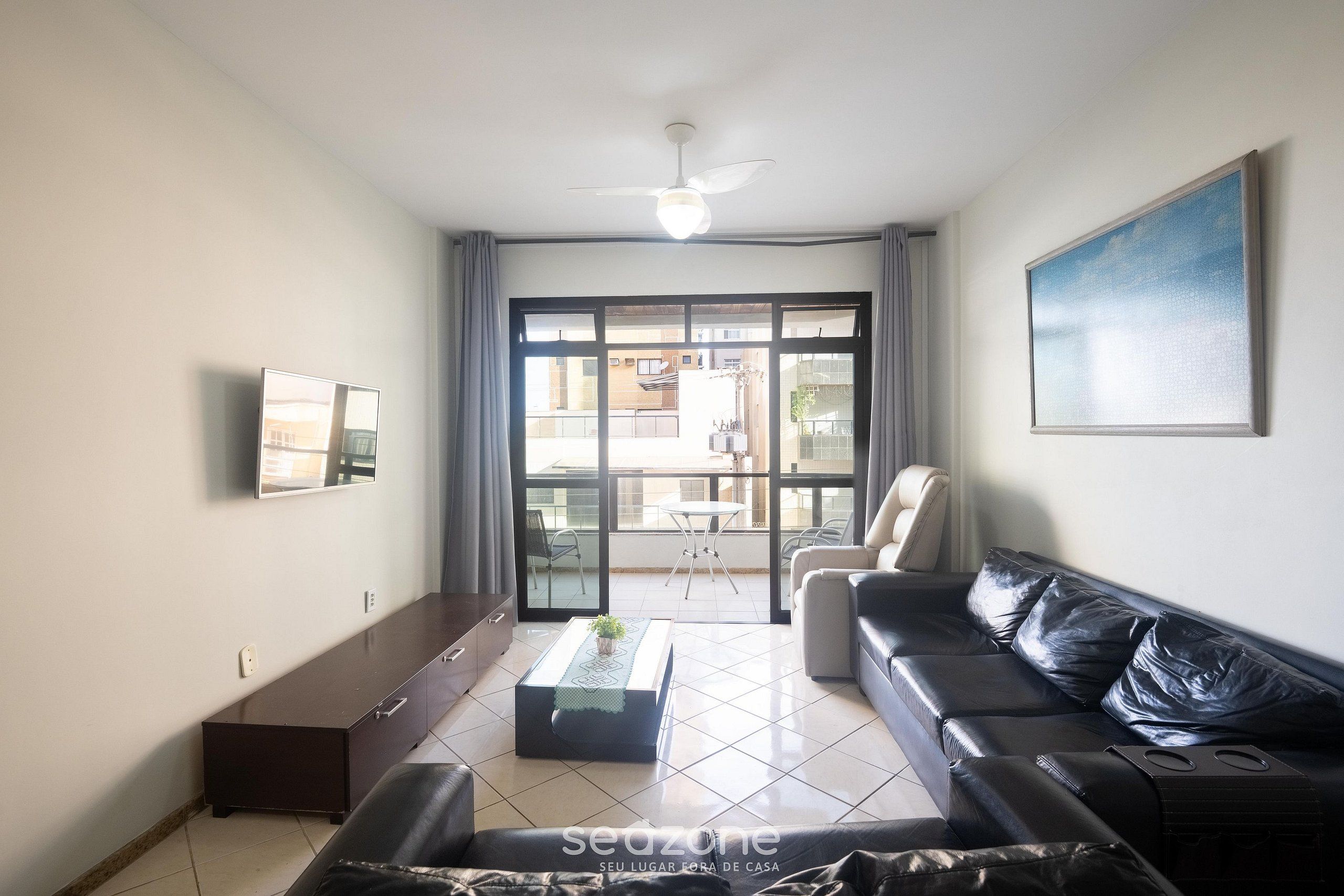 Un salón con sofá, una mesa de centro, televisor y un balcón con vistas.