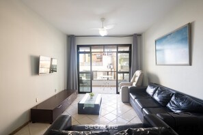A living room with a sofa, a coffee table, a TV, and a balcony with a view. - Apts in a Condominium 130m fr/ Morro Beach - Gfts (Guarapari)
