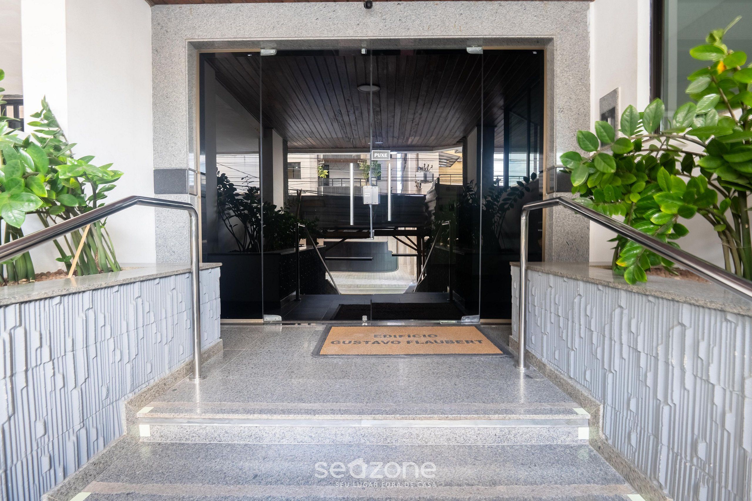 A hotel entrance with a glass door, a doormat, and a metal railing.